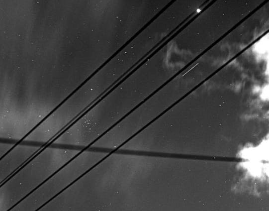 A two-second–long exposure through power and telephone lines shows a white line indicating the X-37B space plane in orbit.